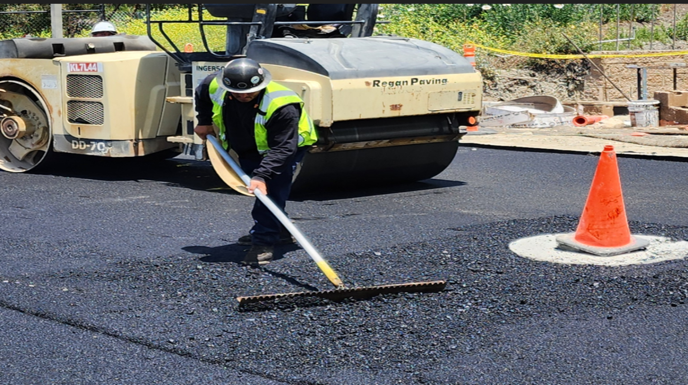 Paving worker manually distributing hot asphalt during construction project.