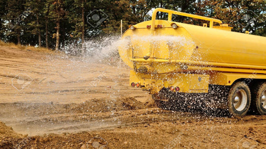 Yellow tanker truck spraying water on a dirt road with trees in the background