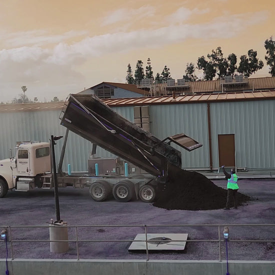 Asphalt being dumped from a dump truck and skip loader bucket at a construction site.