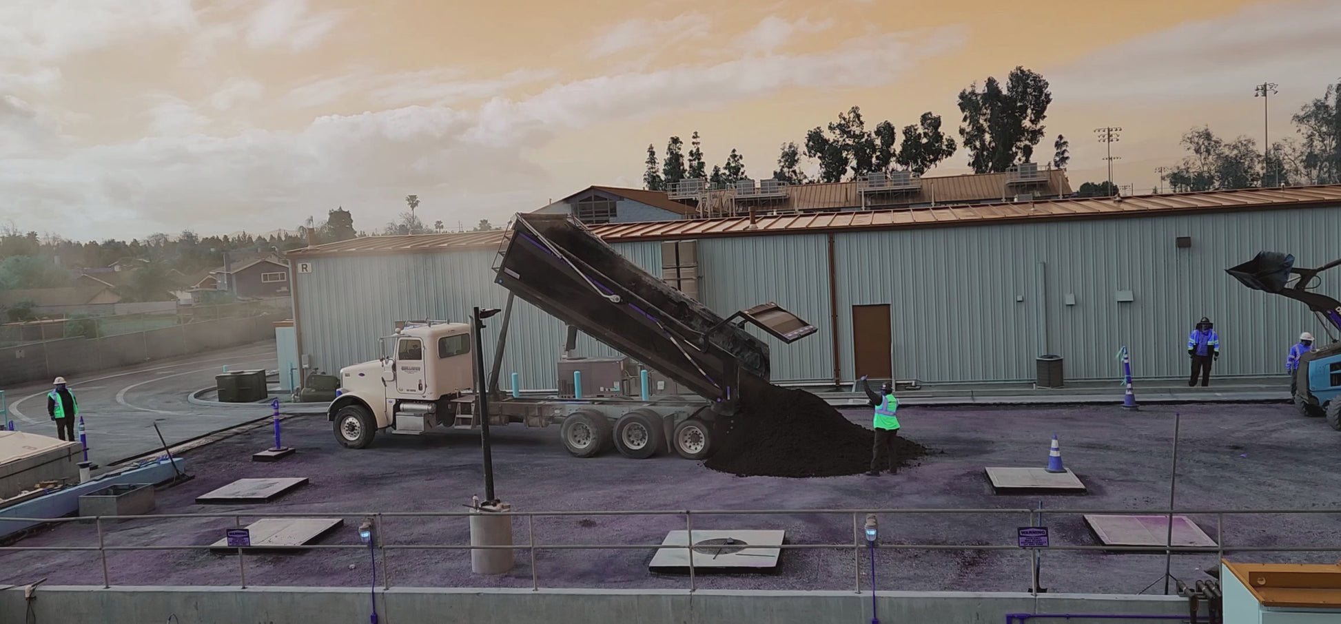 Asphalt being dumped from a dump truck and skip loader bucket at a construction site.